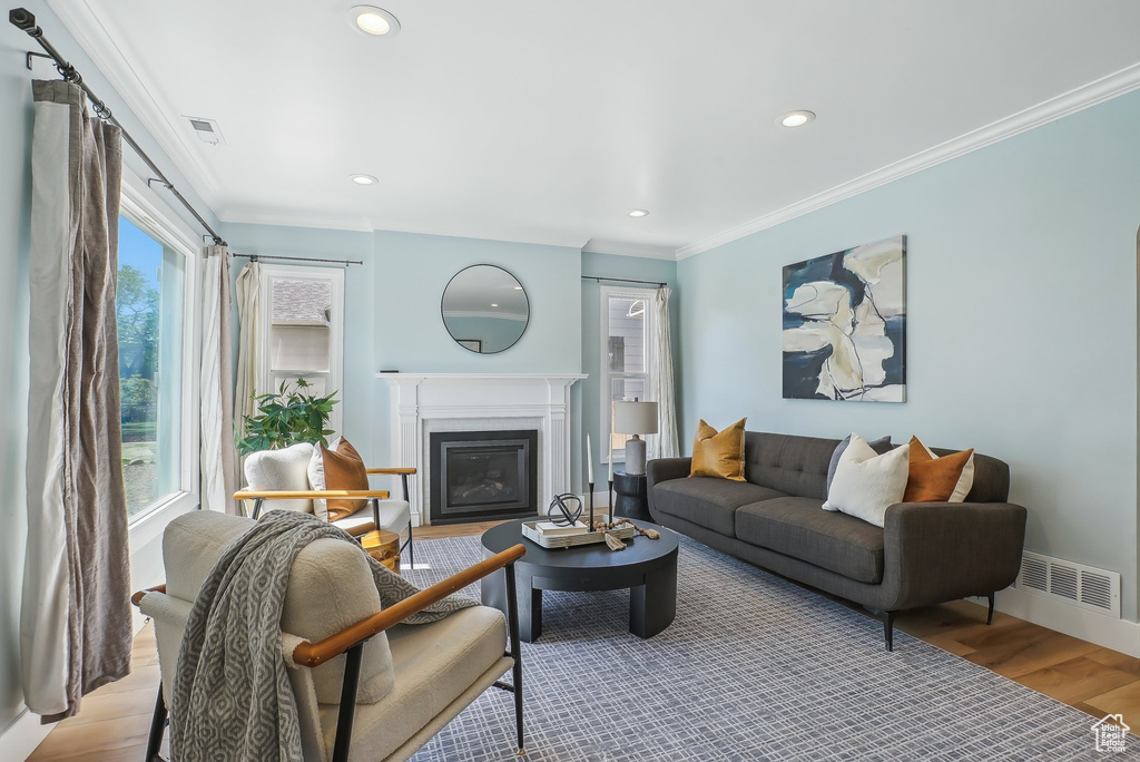 Living room with a glass covered fireplace, crown molding, light wood finished floors, baseboards, and recessed lighting
