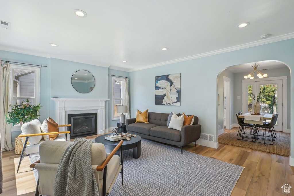 Living area with arched walkways, a fireplace with flush hearth, light wood-style floors, a chandelier, and baseboards
