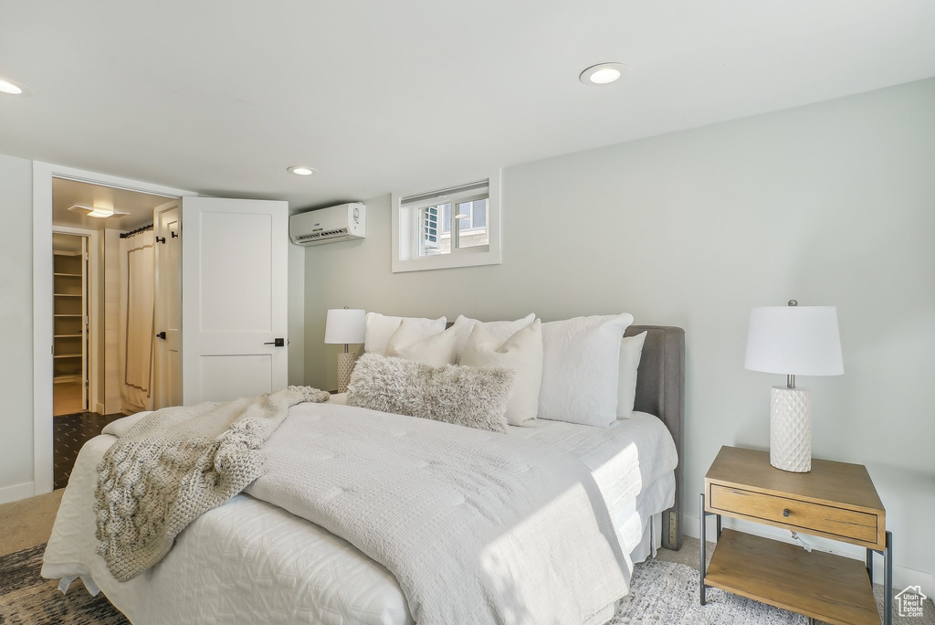 Bedroom with an AC wall unit, light colored carpet, baseboards, recessed lighting, and a walk in closet