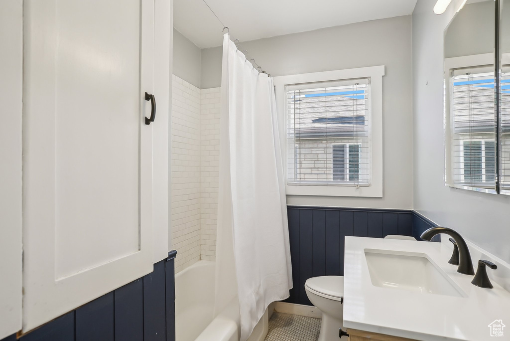 Bathroom with toilet, a wainscoted wall, vanity, shower / bath combination with curtain, and tile patterned floors