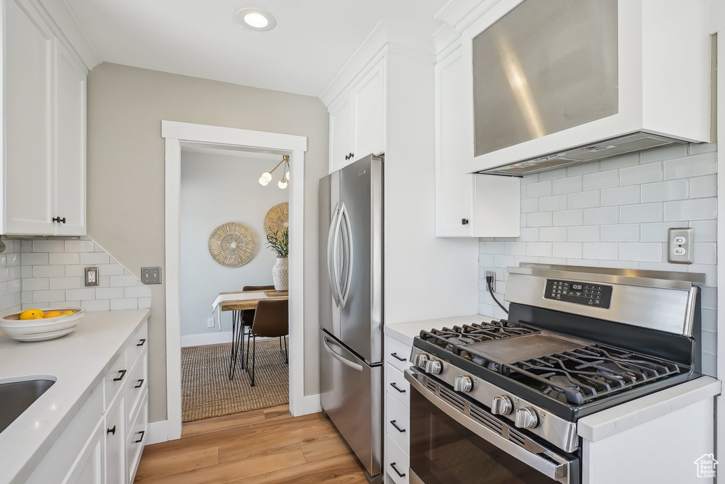 Kitchen with stainless steel appliances, backsplash, light wood-type flooring, light countertops, and white cabinetry