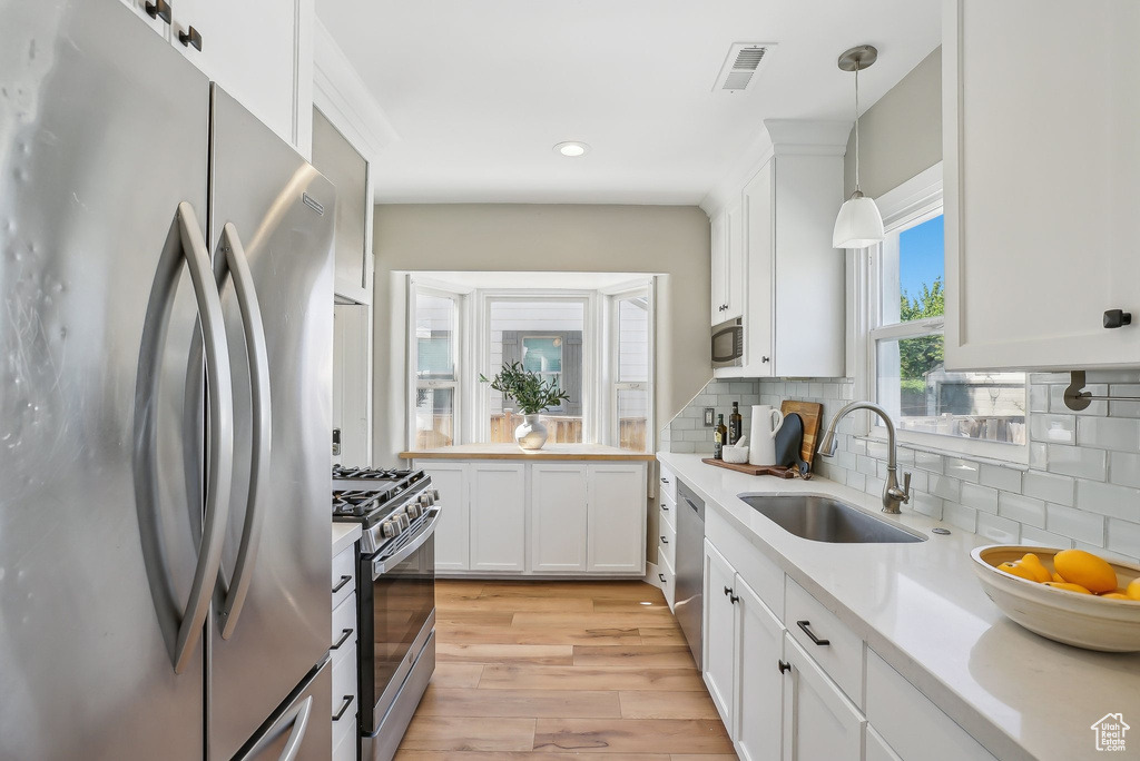 Kitchen featuring stainless steel appliances, a sink, light countertops, light wood-type flooring, and white cabinetry