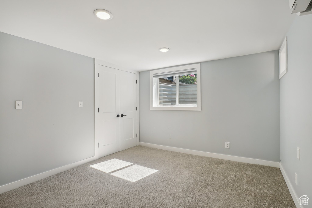 Unfurnished bedroom with light carpet, recessed lighting, baseboards, a wall mounted AC, and a closet