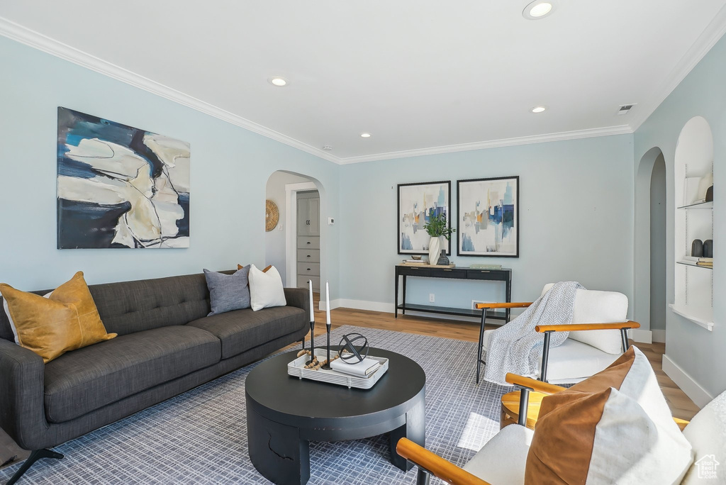 Living area with arched walkways, wood finished floors, ornamental molding, recessed lighting, and baseboards