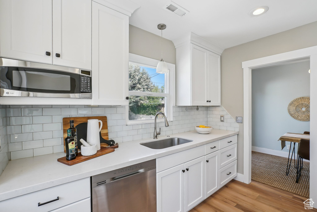 Kitchen featuring appliances with stainless steel finishes, a sink, white cabinets, light wood finished floors, and recessed lighting