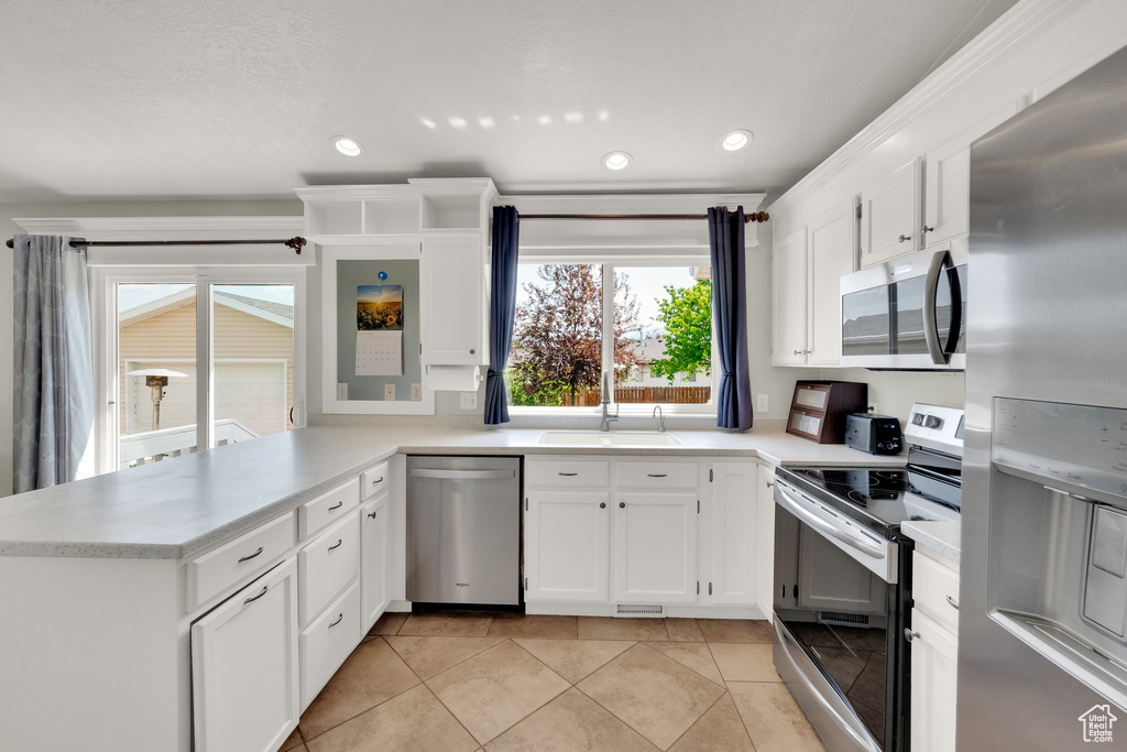 Kitchen with appliances with stainless steel finishes, a sink, a peninsula, light countertops, and recessed lighting