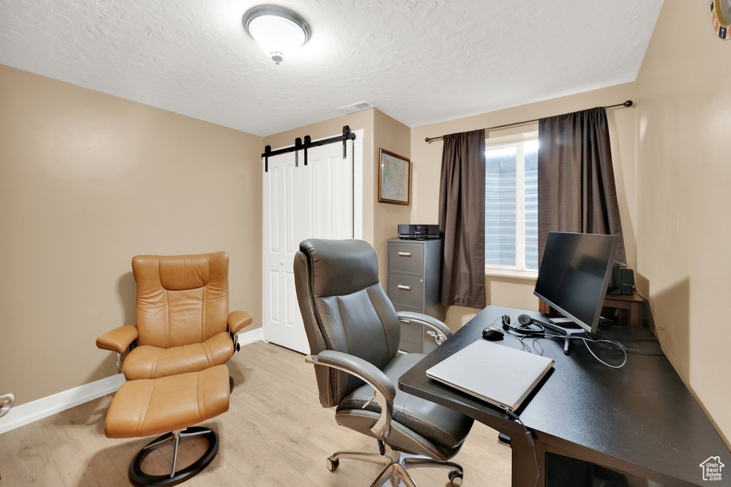 Office area with a textured ceiling, wood finished floors, baseboards, and a barn door