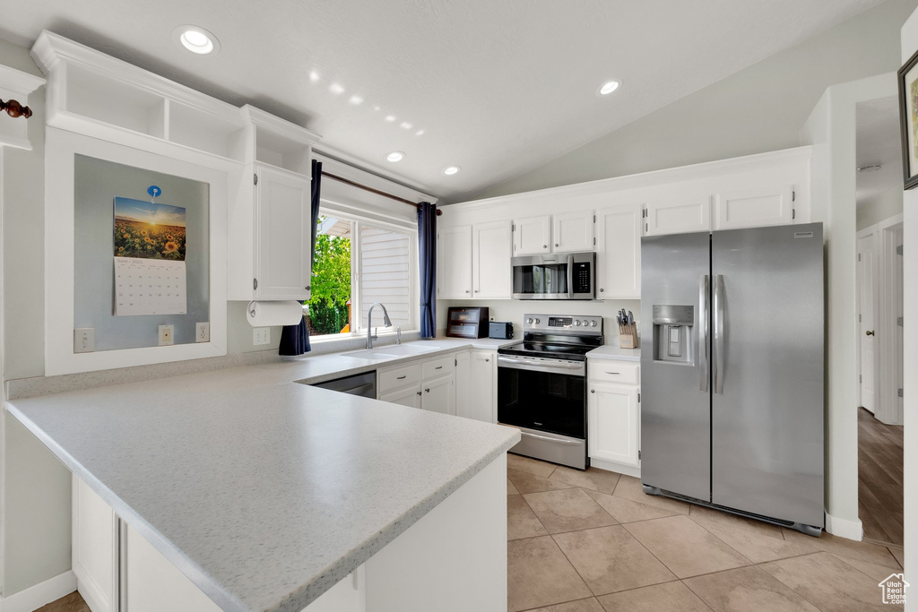 Kitchen featuring stainless steel appliances, a peninsula, a sink, light countertops, and lofted ceiling