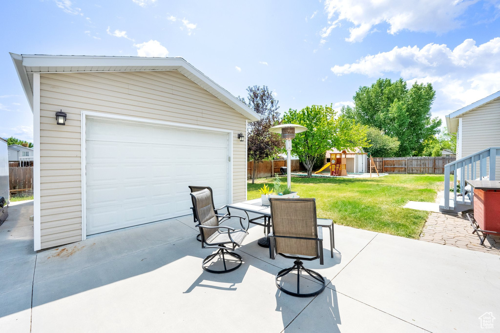 View of patio / terrace with an outdoor structure, a playground, outdoor dining area, and a garage