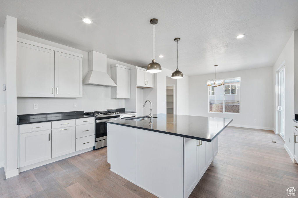 Kitchen with gas range, custom range hood, dark countertops, a sink, and light wood-style flooring