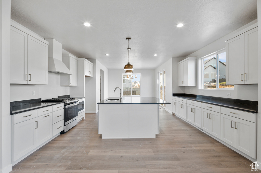 Kitchen featuring stainless steel range with gas cooktop, wall chimney exhaust hood, a sink, dark countertops, and recessed lighting