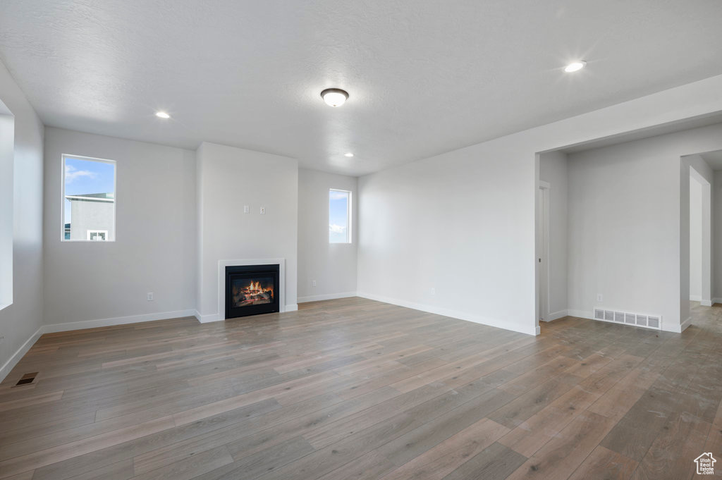 Unfurnished living room with a glass covered fireplace, wood finished floors, baseboards, plenty of natural light, and recessed lighting