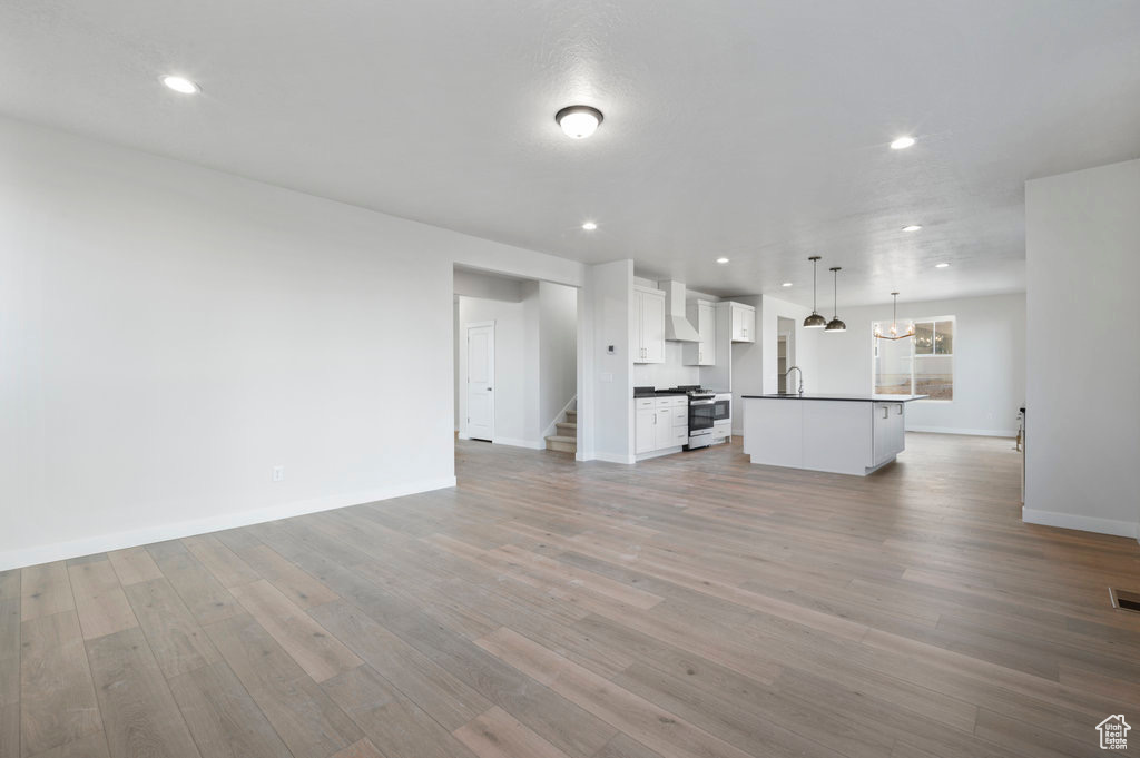 Unfurnished living room with recessed lighting, baseboards, light wood finished floors, a sink, and stairs