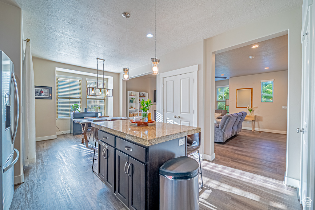 Kitchen featuring stainless steel refrigerator with ice dispenser, light wood-type flooring, a textured ceiling, hanging light fixtures, and baseboards