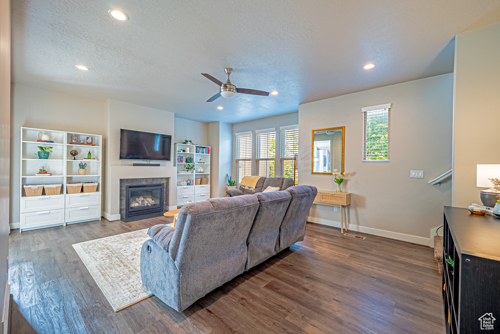 Living room with ceiling fan, a fireplace with flush hearth, a textured ceiling, dark wood-style floors, and baseboards