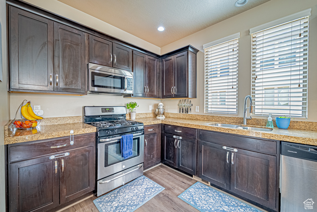 Kitchen with appliances with stainless steel finishes, a sink, dark brown cabinetry, light wood-type flooring, and recessed lighting