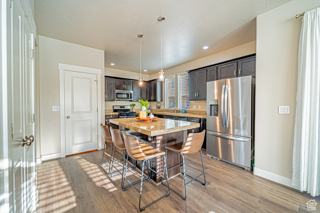 Kitchen featuring appliances with stainless steel finishes, a breakfast bar area, a center island, baseboards, and light wood-style floors