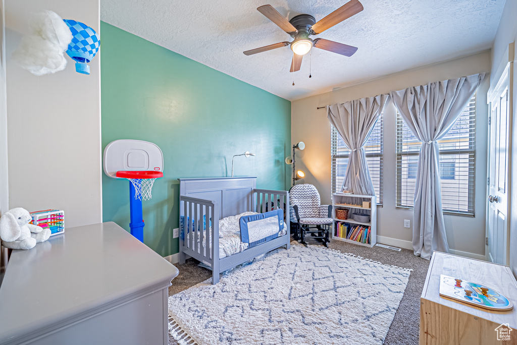 Carpeted bedroom with a crib, a textured ceiling, baseboards, and a ceiling fan
