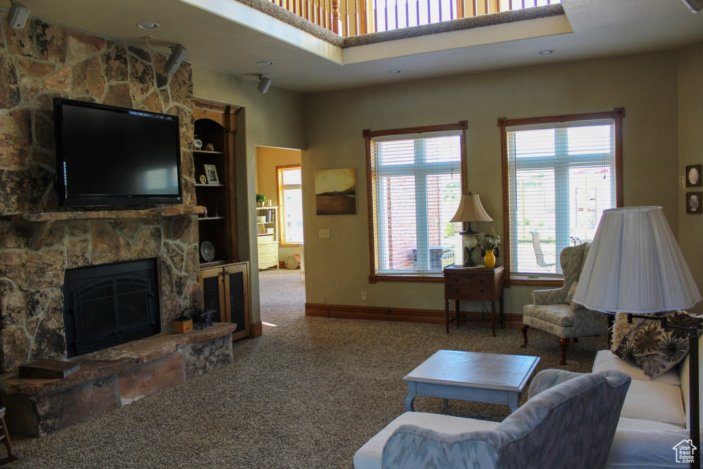 Carpeted living room featuring a stone fireplace and baseboards
