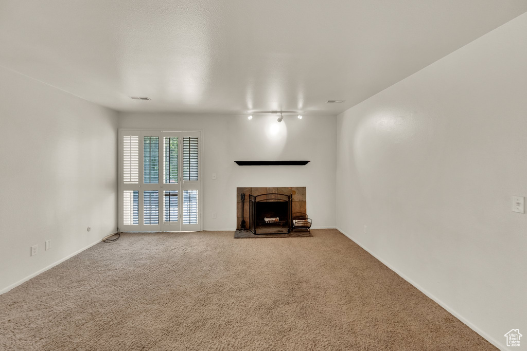 Unfurnished living room featuring carpet floors, a tile fireplace, and baseboards