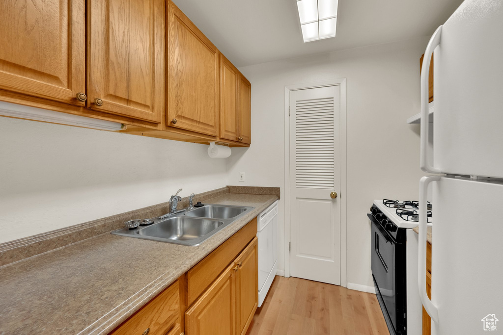 Kitchen with white appliances, a sink, and light wood-type flooring
