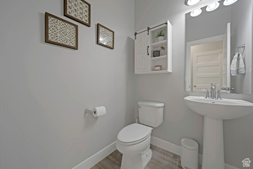 Bathroom with toilet, baseboards, wood finished floors, and a sink