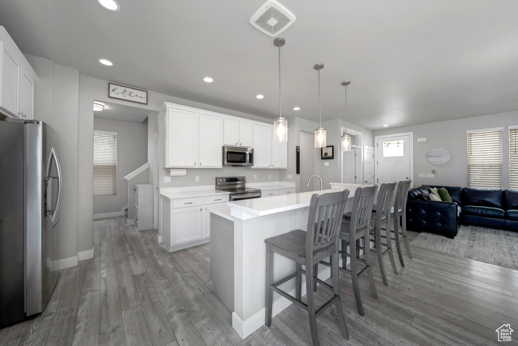 Kitchen with appliances with stainless steel finishes, light wood-type flooring, baseboards, white cabinets, and recessed lighting