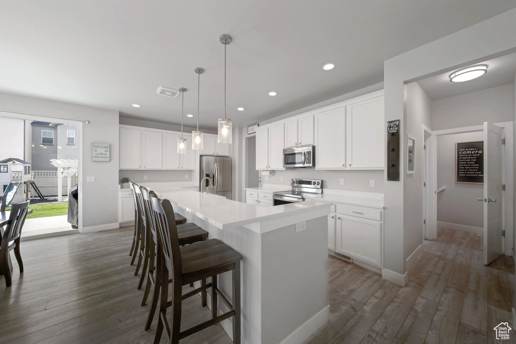 Kitchen with appliances with stainless steel finishes, a spacious island, dark wood finished floors, white cabinetry, and recessed lighting