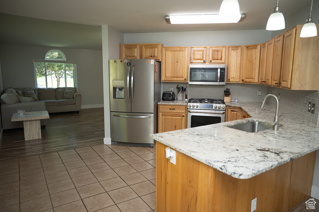 Kitchen with appliances with stainless steel finishes, light stone counters, backsplash, light tile patterned flooring, and a peninsula