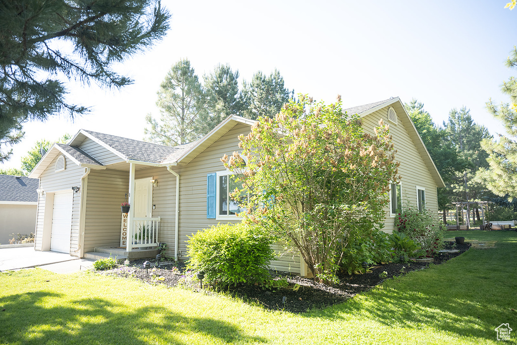 View of front facade featuring a garage, a front yard, a shingled roof, and driveway