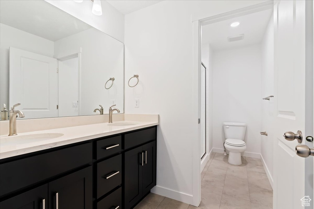 Bathroom featuring toilet, double vanity, a stall shower, and baseboards