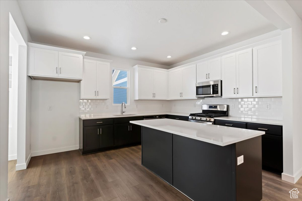 Kitchen featuring appliances with stainless steel finishes, a sink, white cabinets, a kitchen island, and tasteful backsplash