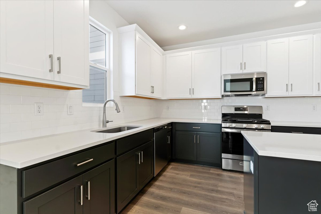 Kitchen with appliances with stainless steel finishes, a sink, white cabinetry, light countertops, and wood finished floors