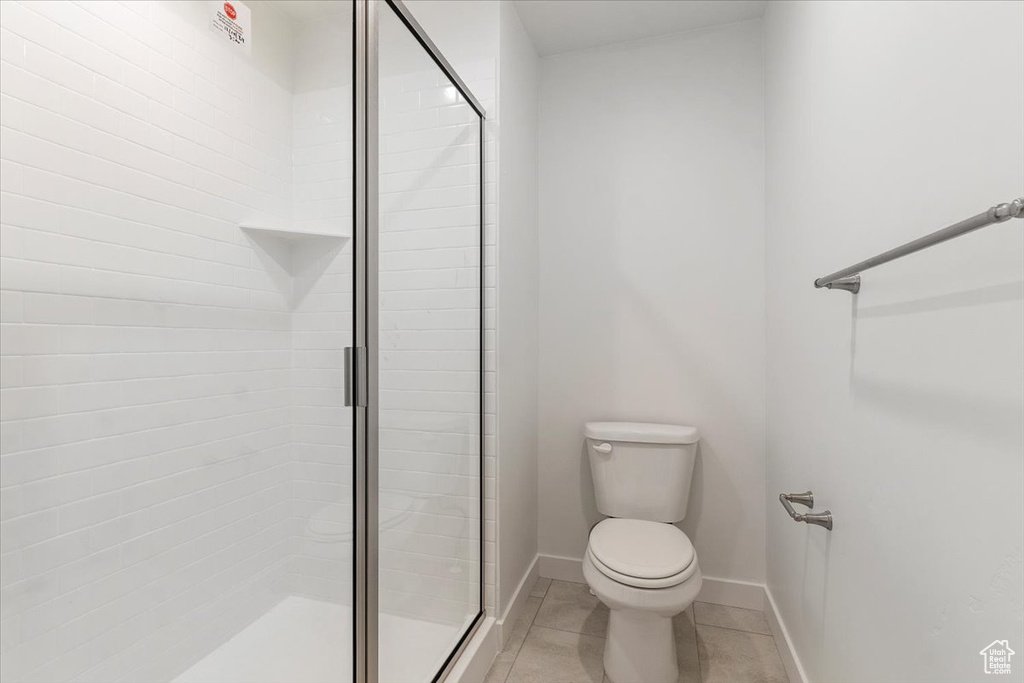 Bathroom with toilet, a stall shower, baseboards, and tile patterned flooring