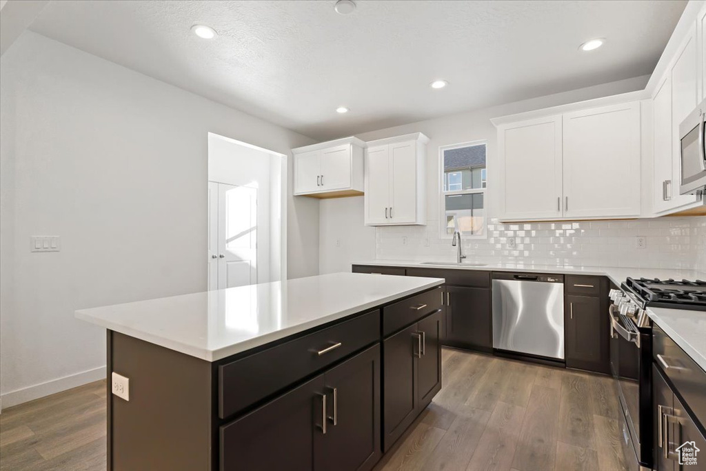 Kitchen featuring appliances with stainless steel finishes, decorative backsplash, wood finished floors, white cabinetry, and light countertops