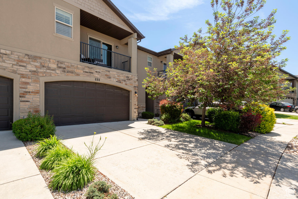 View of front of house with stone siding, stucco siding, a garage, concrete driveway, and a balcony