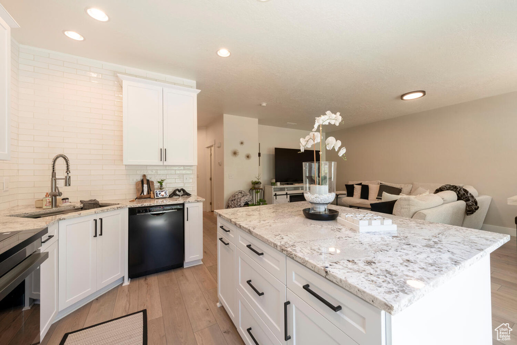 Kitchen featuring dishwasher, a sink, open floor plan, a center island, and light wood-style floors
