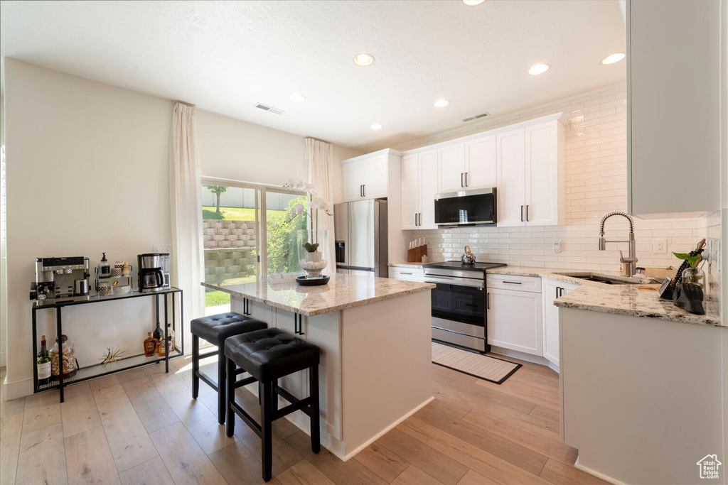 Kitchen with appliances with stainless steel finishes, a sink, a center island, a kitchen bar, and backsplash