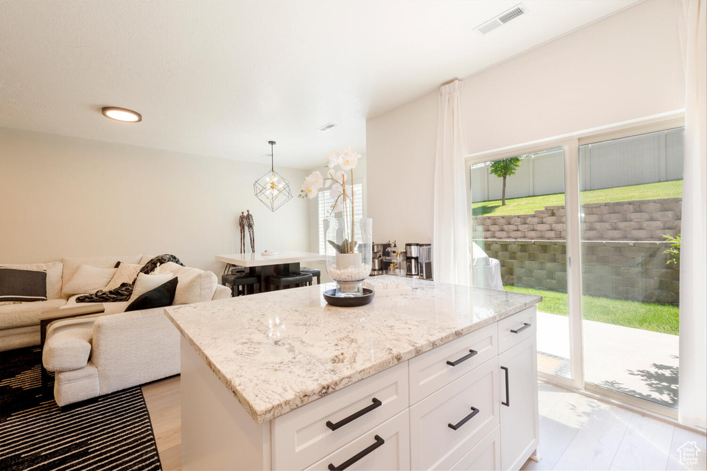 Kitchen featuring light stone countertops, open floor plan, white cabinets, decorative light fixtures, and a center island