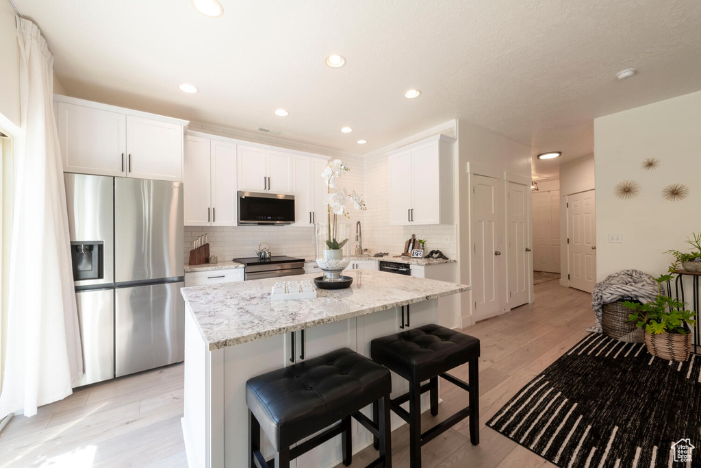 Kitchen with appliances with stainless steel finishes, tasteful backsplash, a kitchen island, white cabinetry, and light stone counters