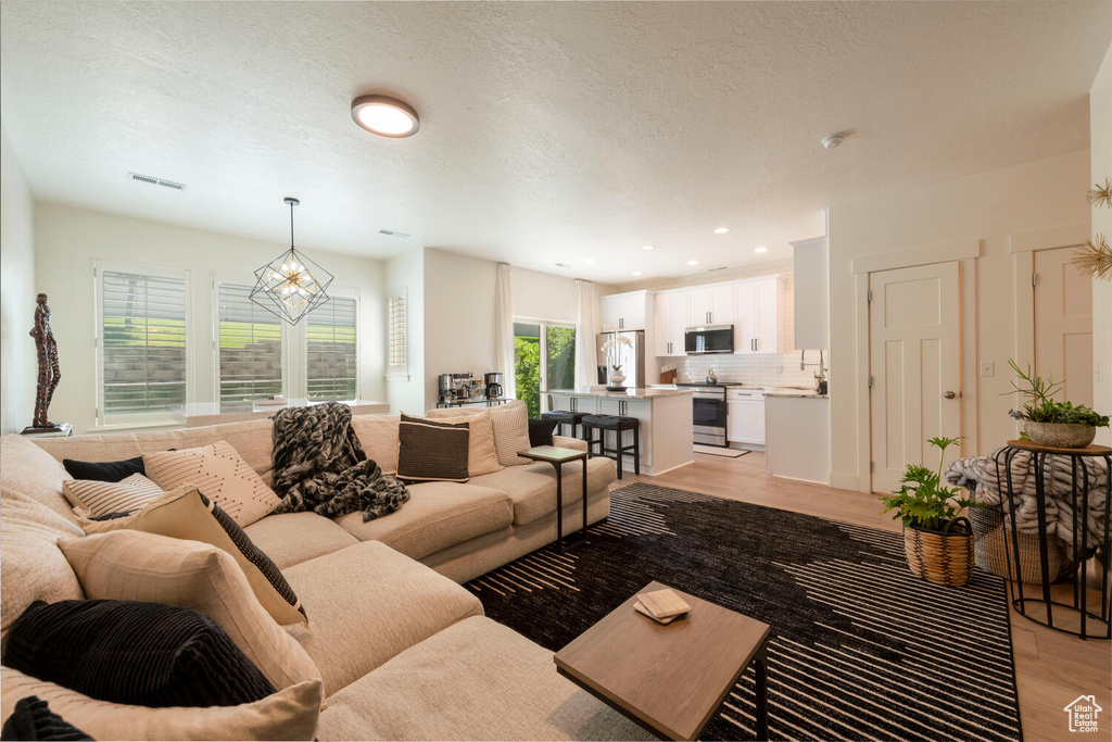 Living area with light wood-type flooring, a chandelier, a textured ceiling, and recessed lighting