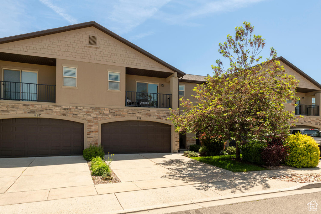 View of property featuring stucco siding, driveway, an attached garage, and stone siding