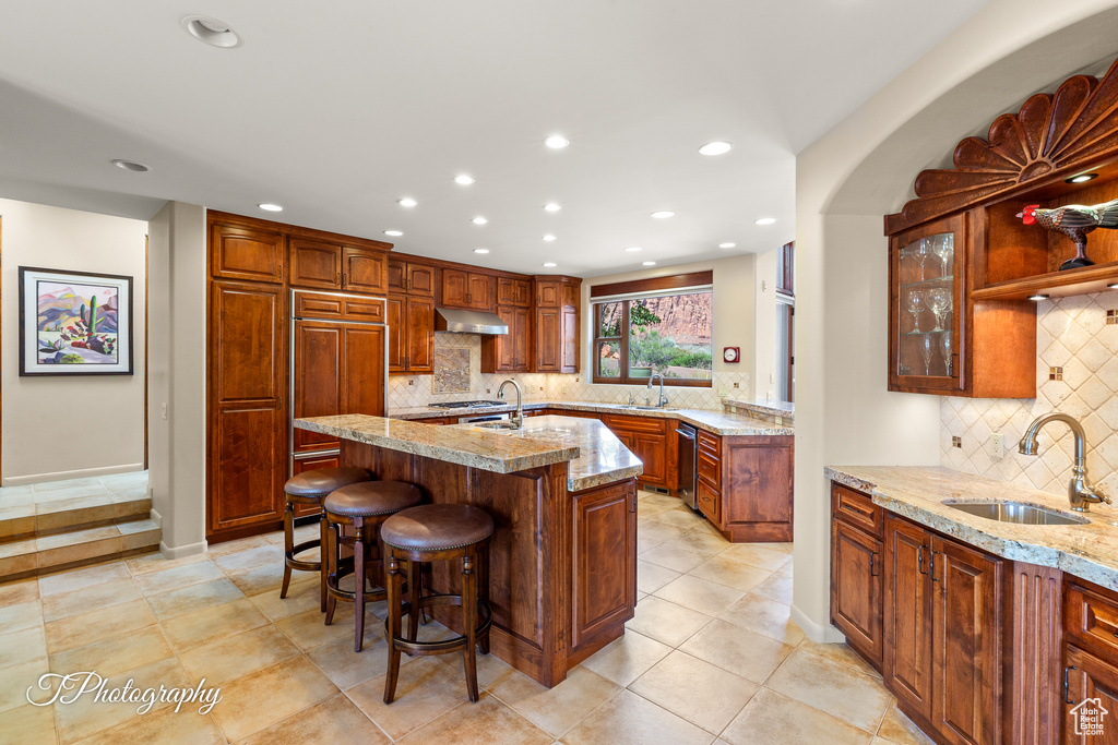 Kitchen with a sink, recessed lighting, decorative backsplash, light stone counters, and a kitchen breakfast bar