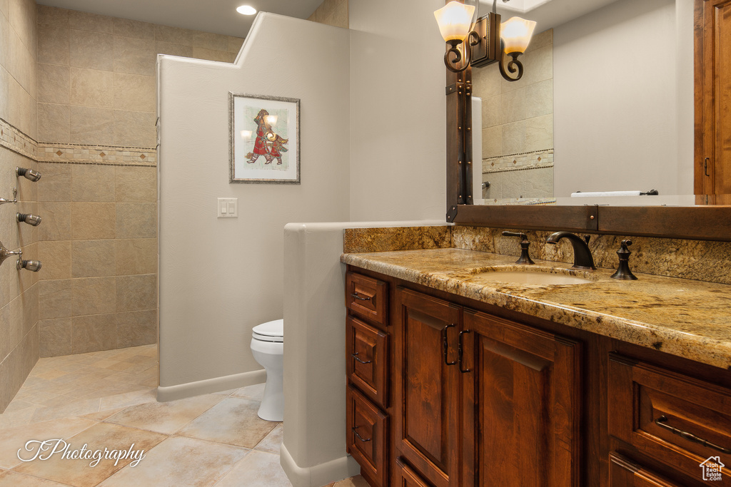 Bathroom with vanity, toilet, tiled shower, tile patterned floors, and baseboards