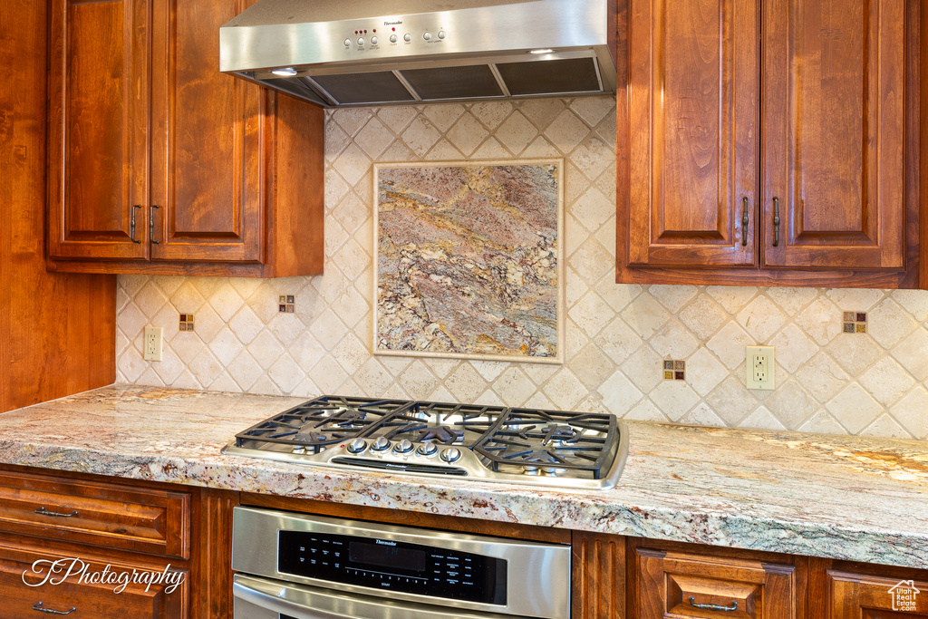 Kitchen with ventilation hood, stainless steel appliances, tasteful backsplash, and light stone counters