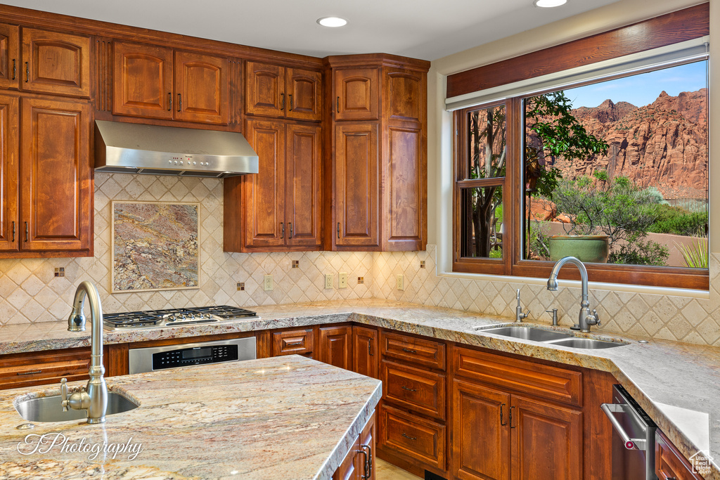 Kitchen with under cabinet range hood, a sink, appliances with stainless steel finishes, tasteful backsplash, and light stone countertops