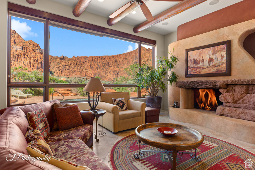 Living room with a mountain view, beamed ceiling, plenty of natural light, light tile patterned flooring, and a ceiling fan