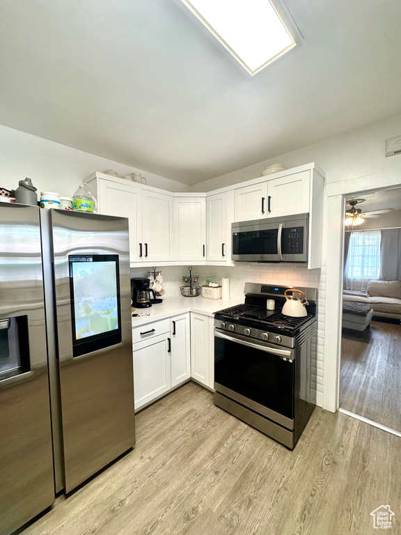 Kitchen with appliances with stainless steel finishes, white cabinets, light wood finished floors, tasteful backsplash, and light countertops