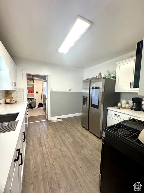 Kitchen with black range with gas cooktop, white cabinets, light countertops, light wood-style floors, and tasteful backsplash