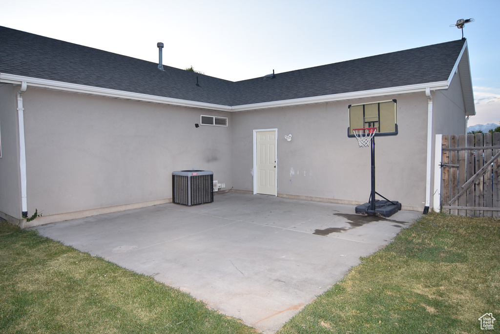 Rear view of house featuring cooling unit, roof with shingles, stucco siding, and a patio